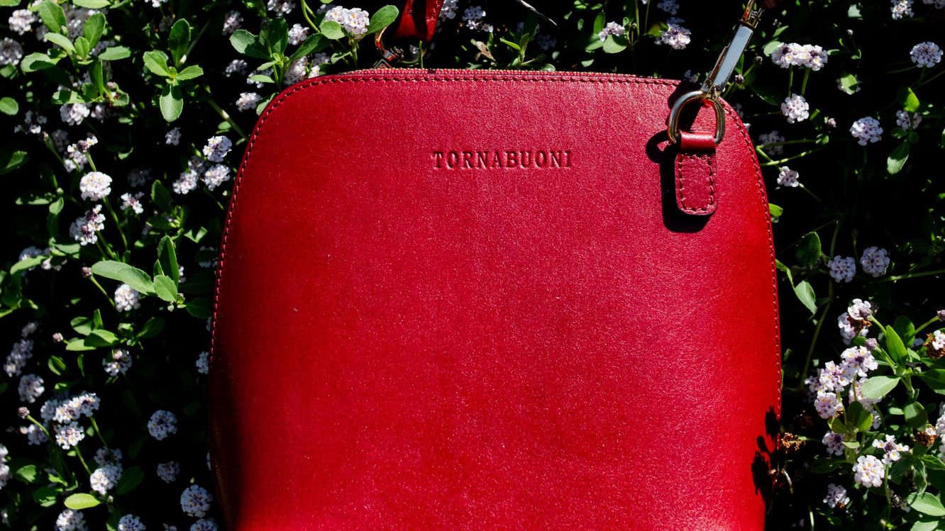 Red Tornabuoni leather crossbody bag resting among white flowers