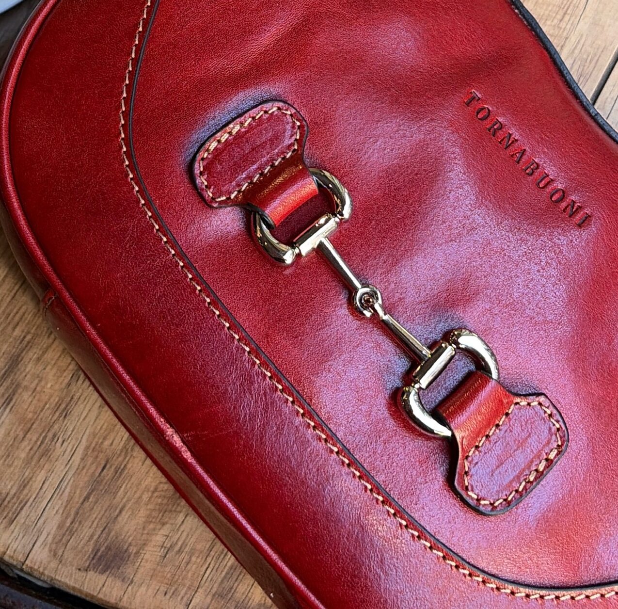 Close-up of a red Tornabuoni vegetable-tanned Italian leather bag showing hand stitching, burnished edges and the embossed Tornabuoni name